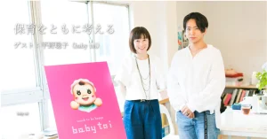 女性と男性がピンクのポスターの前で対談している様子