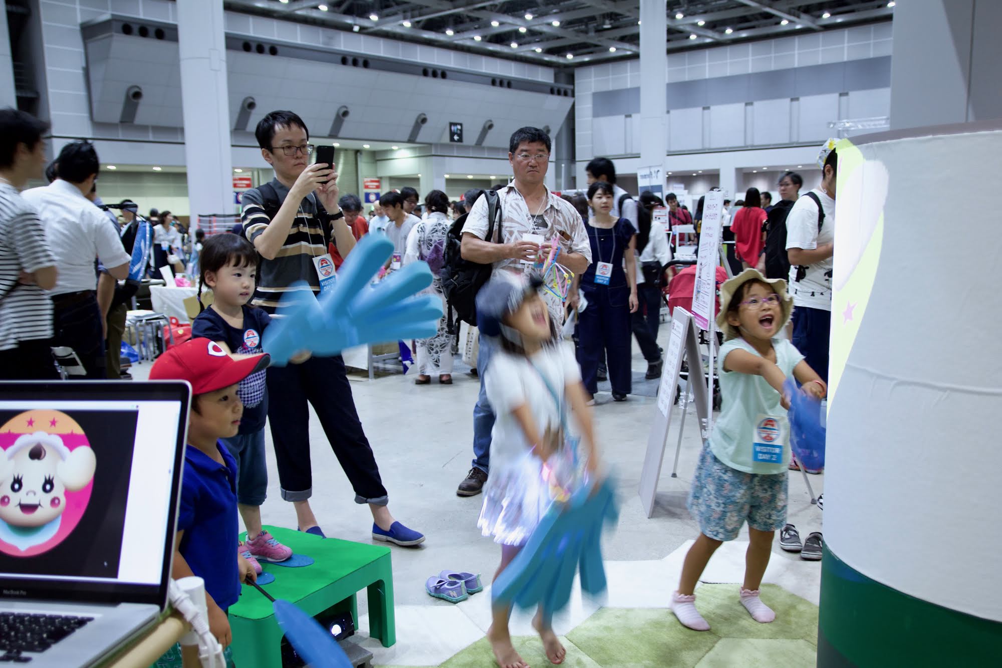青いビッグハンドで遊ぶ子どもたちとスマホを操作する大人