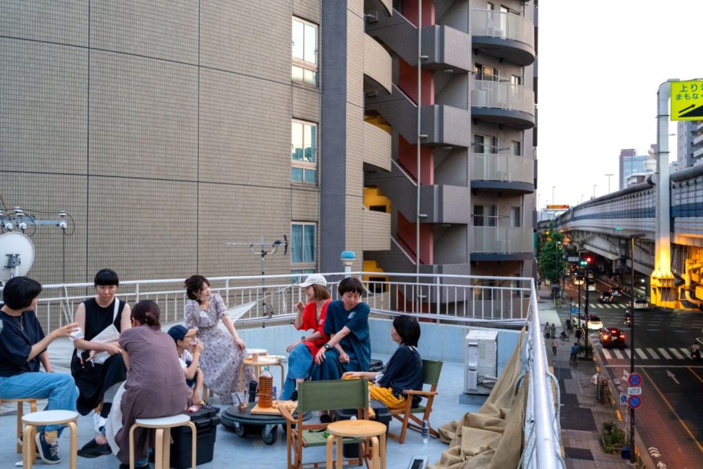 屋上で談笑する大人たちと夕暮れの街並み