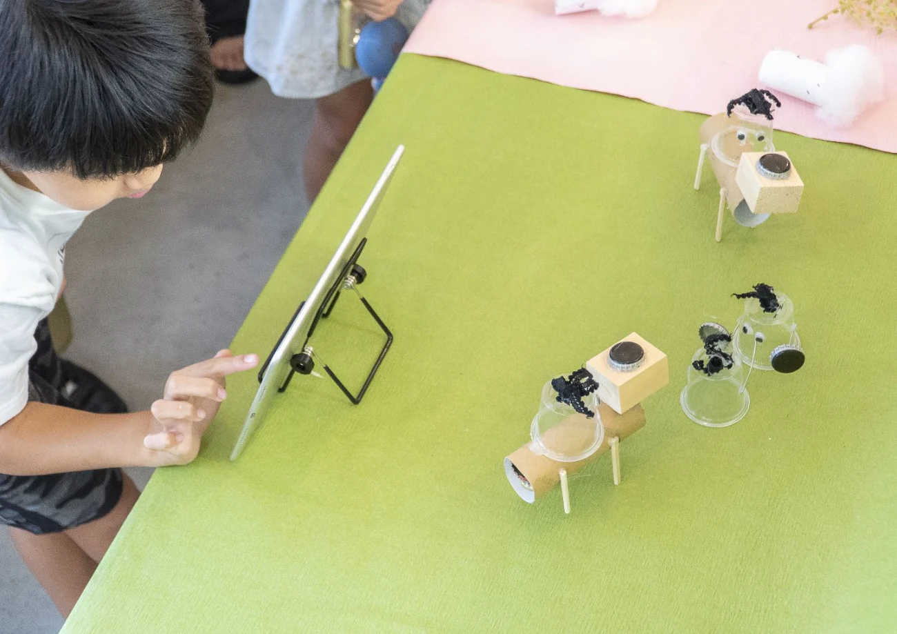 子どもがタブレットを操作し、工作したロボットを動かしている